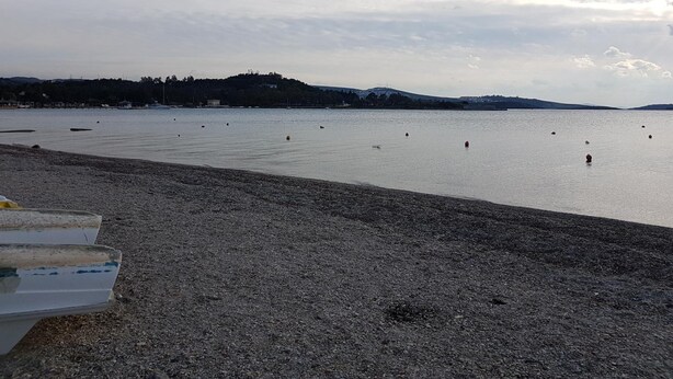 A pebbly beach with calm water, a distant hill, and a clear sky. - Limon Pansiyon (Foça)