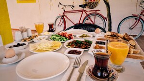 A breakfast table with various dishes, a glass of orange juice, and a red bicycle in the background. - Limon Pansiyon (Foça)