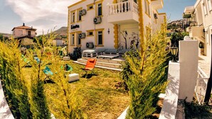 A multi-story building with balconies, air conditioning units, and a garden area with outdoor furniture. - Limon Pansiyon (Foça)