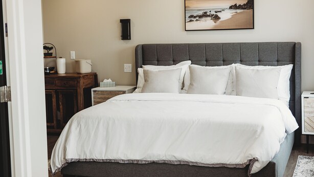 A neatly made bed with white linens and a gray headboard in a hotel room. - Riverside Suites (Grand Falls - Windsor)