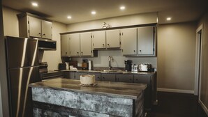 A modern kitchen with a large island, stainless steel appliances, and light-colored cabinetry. - Riverside Suites (Grand Falls - Windsor)