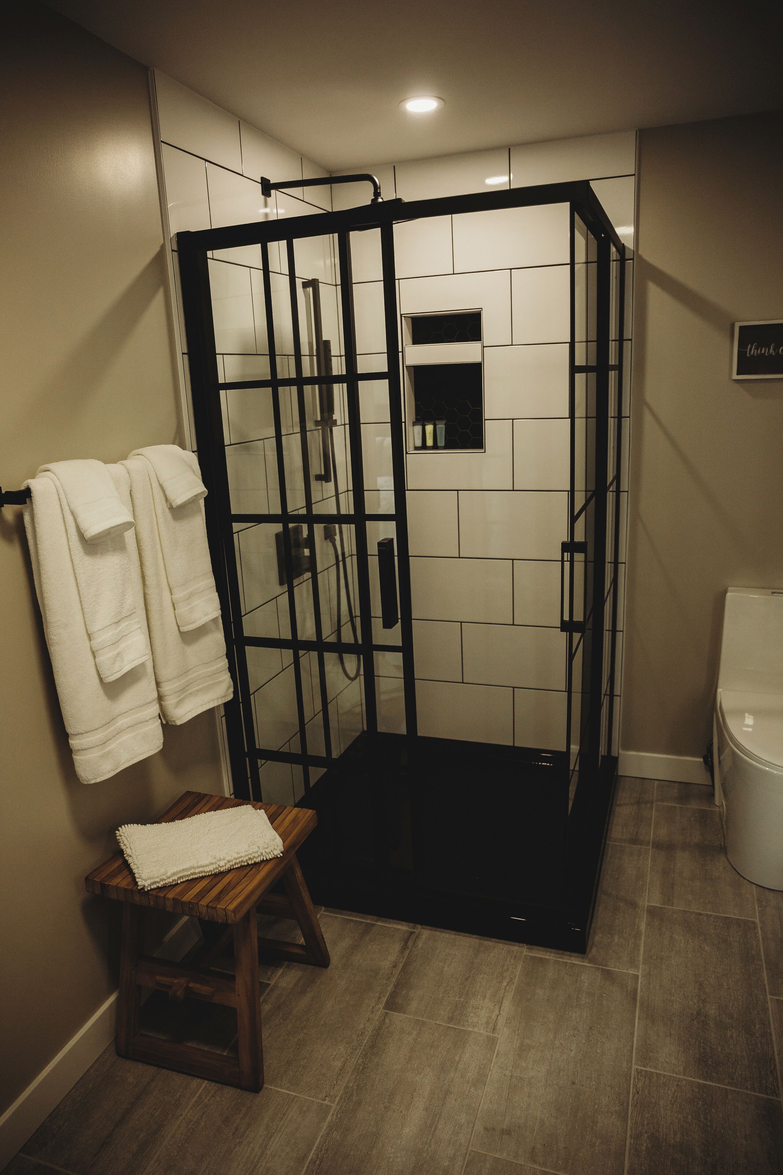 Zona de ducha con mampara de vidrio, banco de madera y un inodoro.