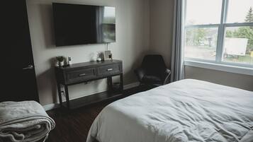 Een slaapkamer met een bed, een aan de muur bevestigde televisie, een stoel en een raam met uitzicht op buiten.
