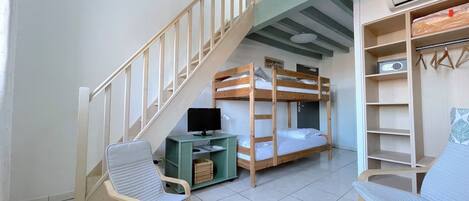 Een kamer met stapelbedden, een bureau met een computer, twee stoelen, een trap en een garderobe met kledinghangers.