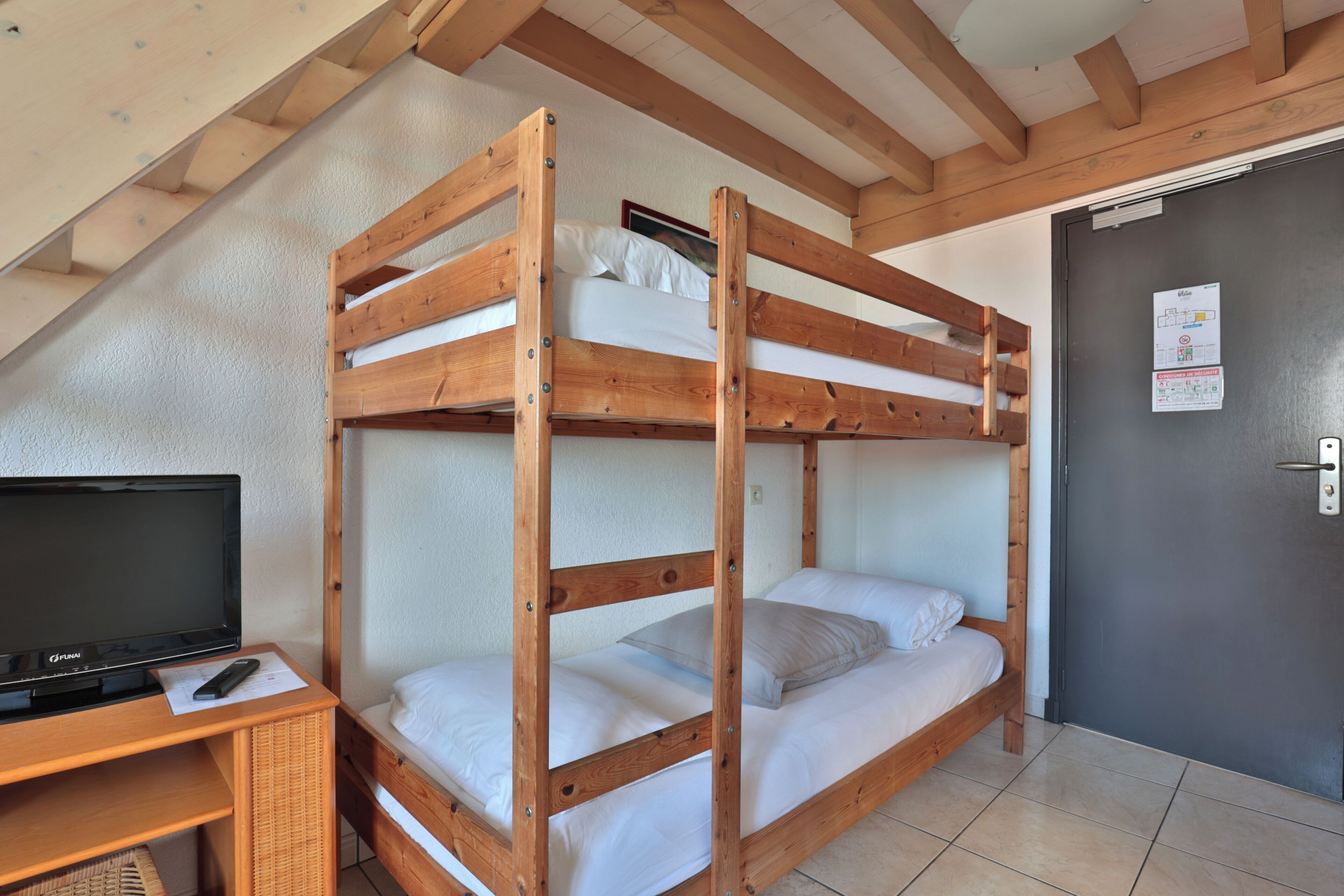 Een slaapkamer met stapelbed, een televisie op een houten standaard, een deur met een bericht en een betegelde vloer.