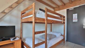 Een slaapkamer met stapelbed, een televisie op een houten standaard, een deur met een bericht en een betegelde vloer.