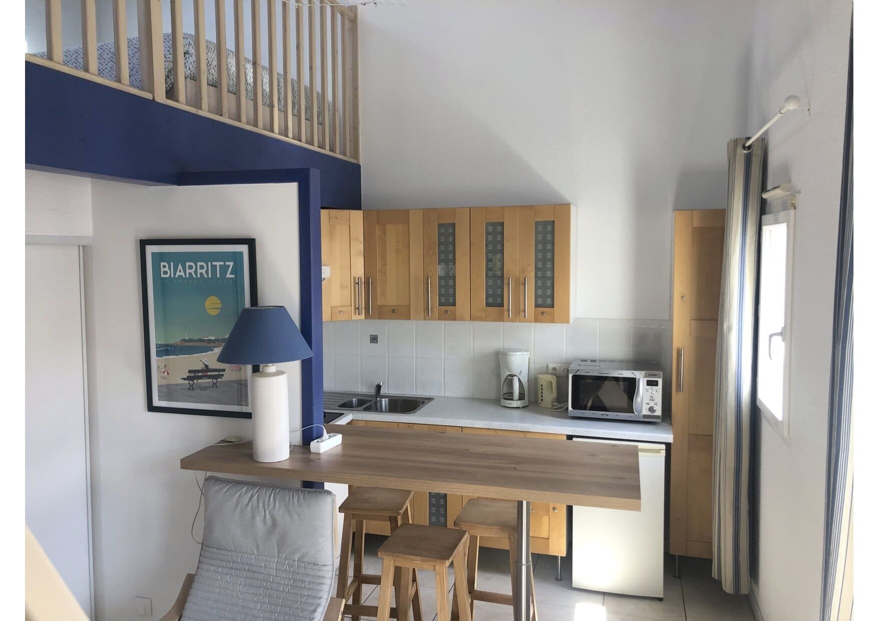 Cocina compacta con armarios de madera, microondas, cafetera y una pequeña isla con taburetes.
