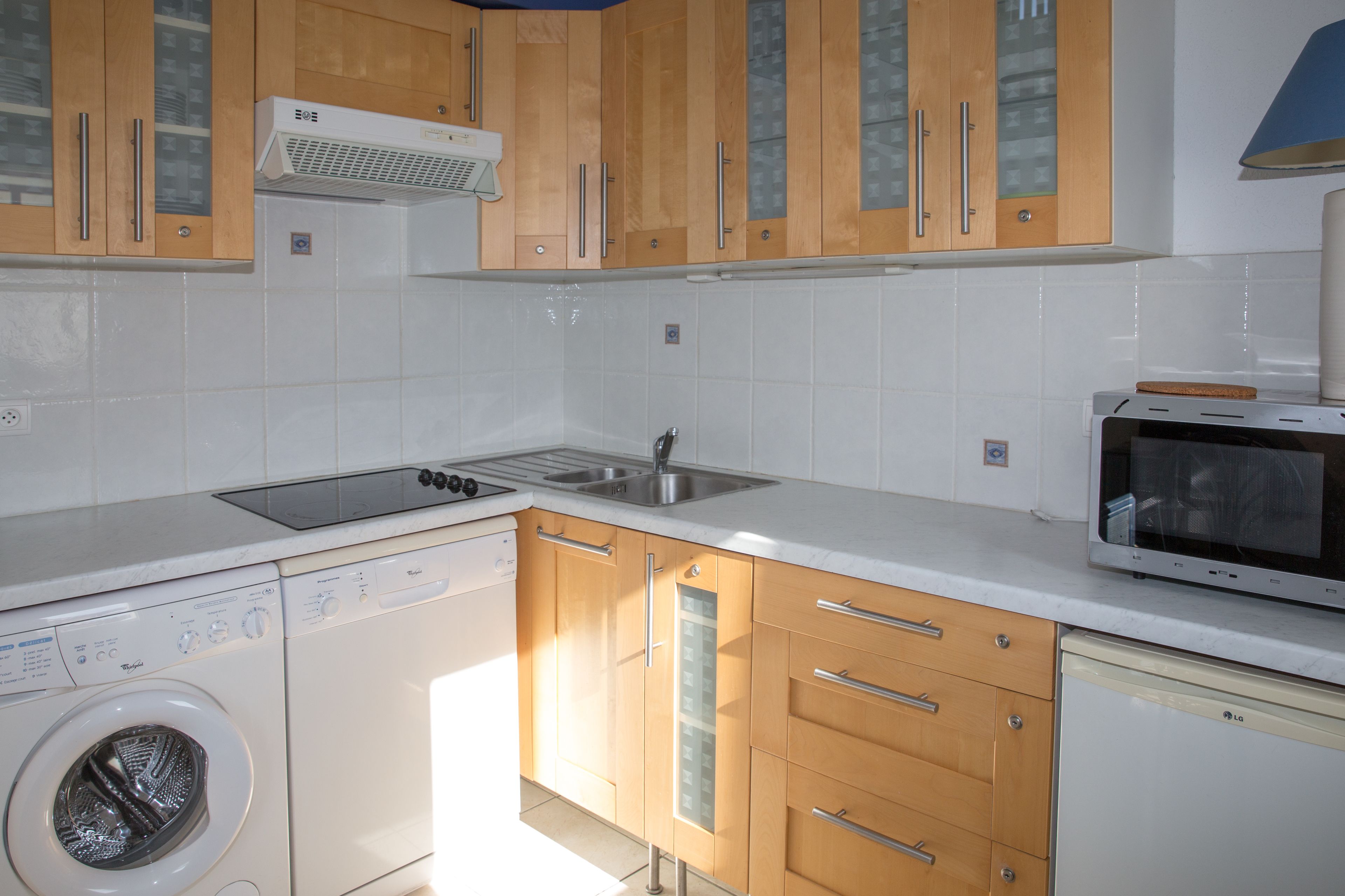 A compact kitchen with wooden cabinets, a built-in microwave, a washing machine, and a dishwasher.