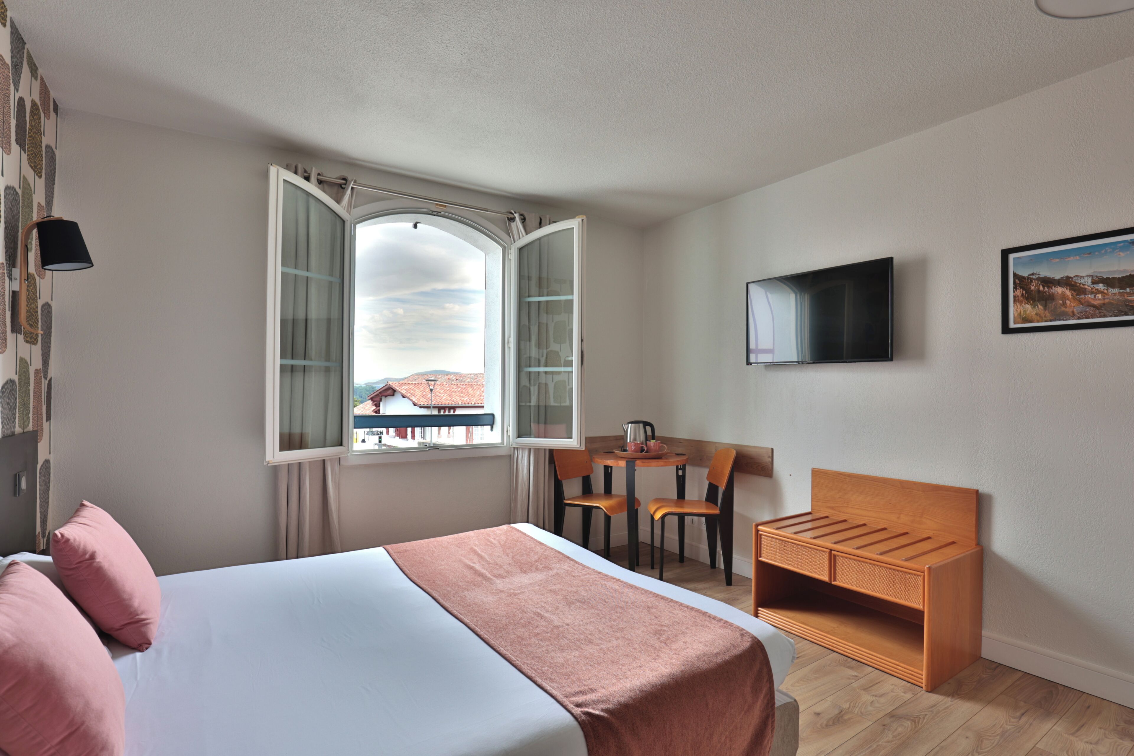 Habitación de hotel con cama, escritorio con sillas, televisor y ventana con vistas.