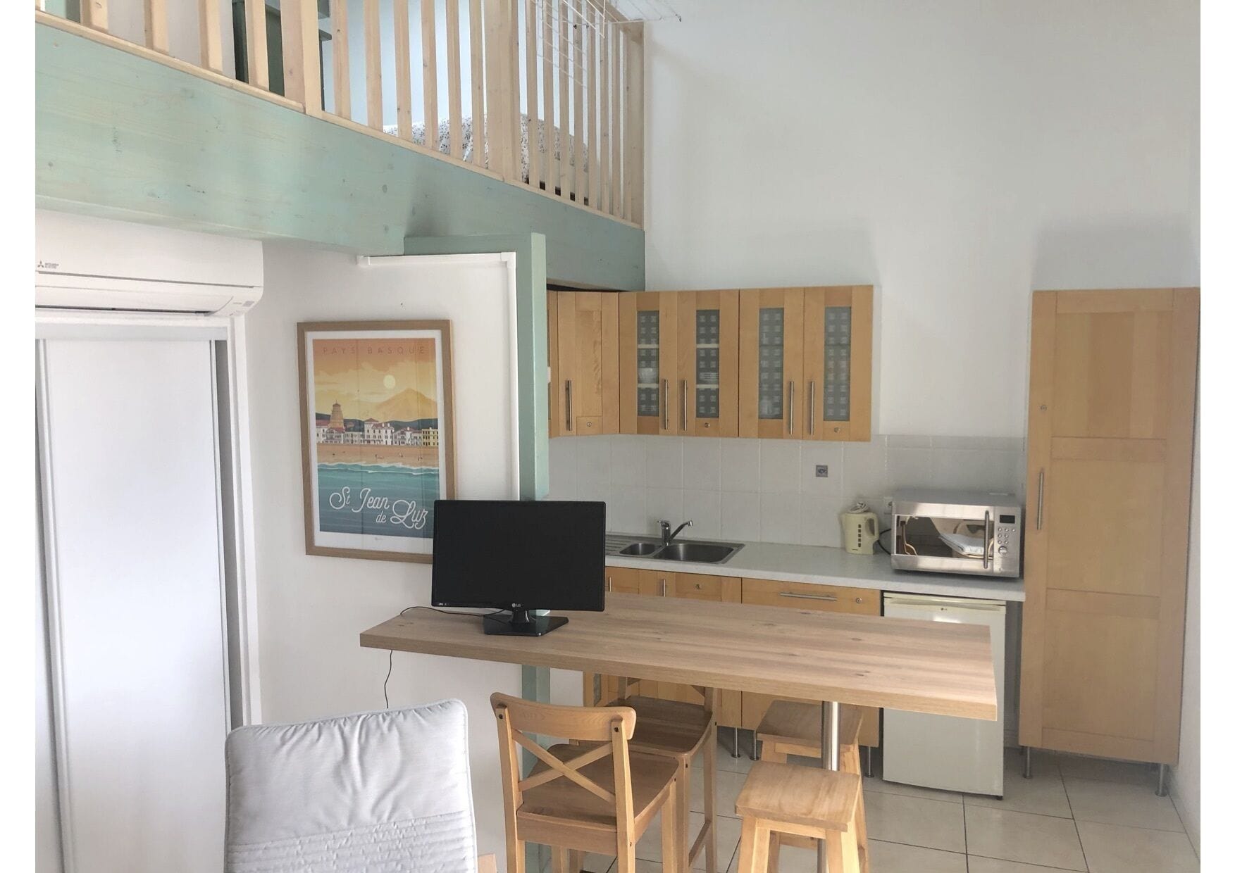 Een kleine keuken met houten kastjes, een magnetron en een eethoek met een tafel en stoelen.