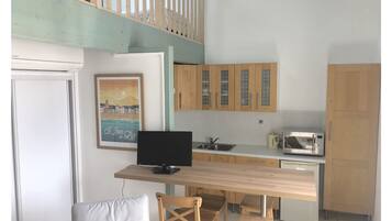Een kleine keuken met houten kastjes, een magnetron en een eethoek met een tafel en stoelen.