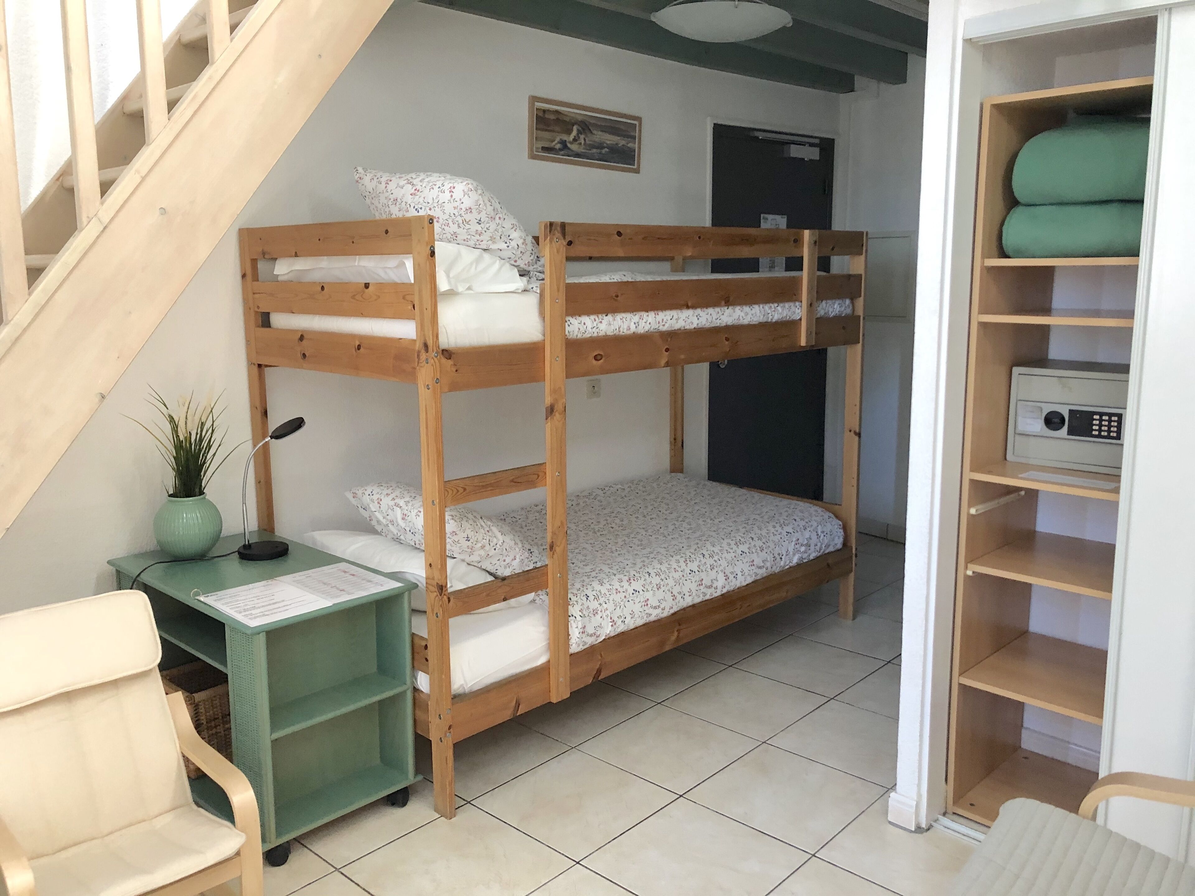 Habitación con literas, un escritorio, una silla y un estante verde.