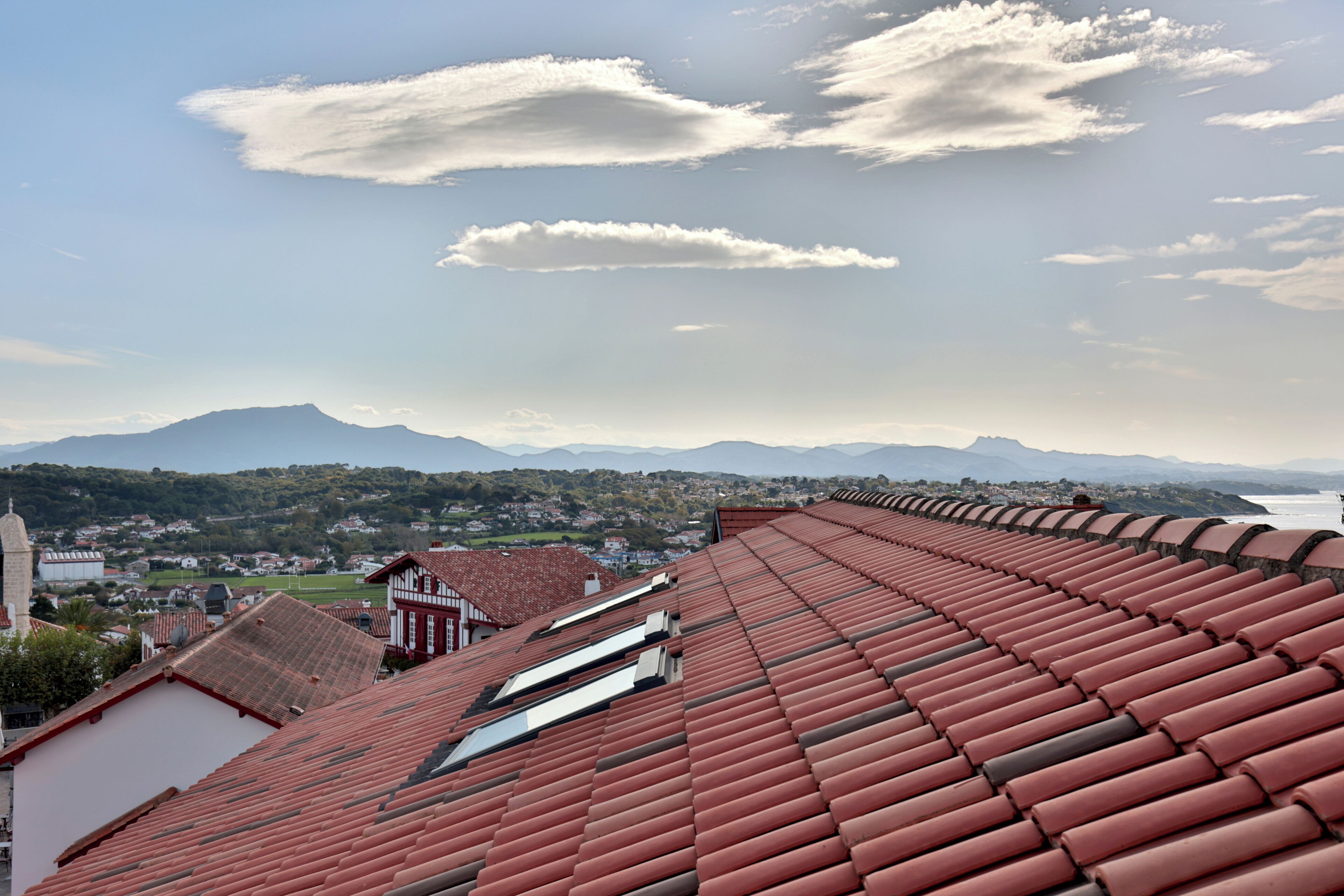 A rooftop with red tiles, a view of a town, and distant mountains.