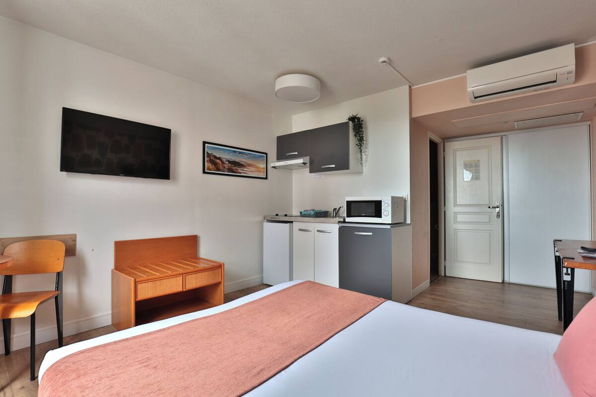 A hotel room with a bed, a desk, a chair, a microwave, and a wardrobe.