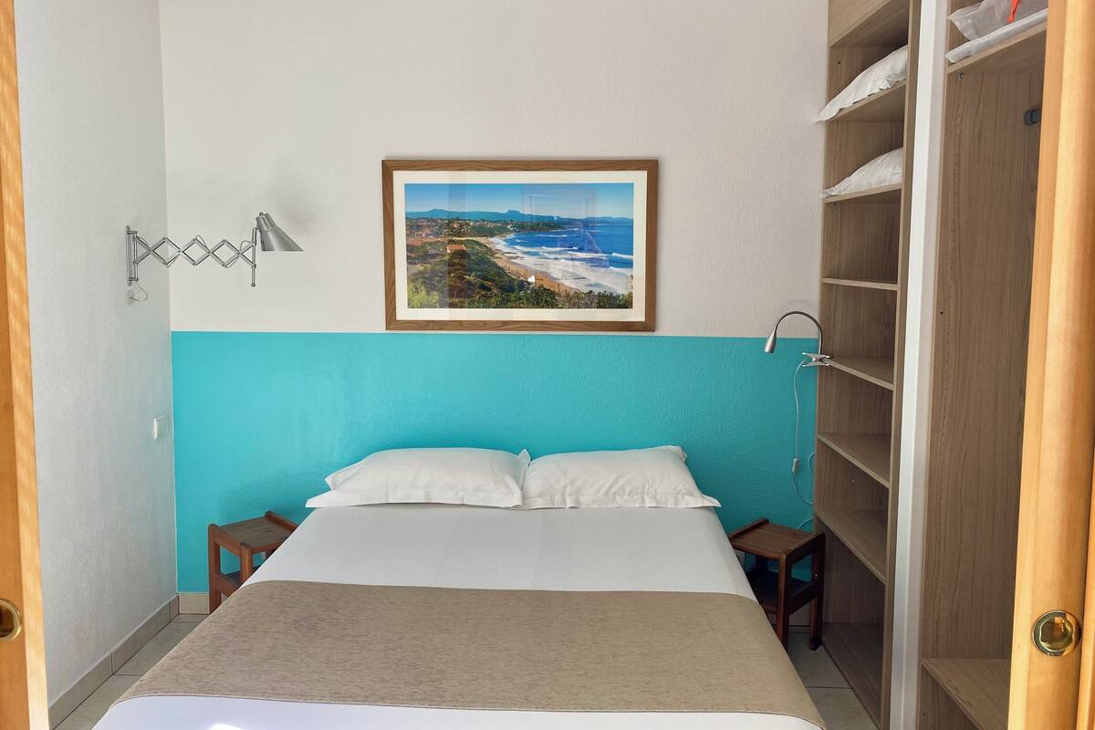A hotel room with a bed, a nightstand, a wooden wardrobe, a framed picture on the wall, and a towel rack.
