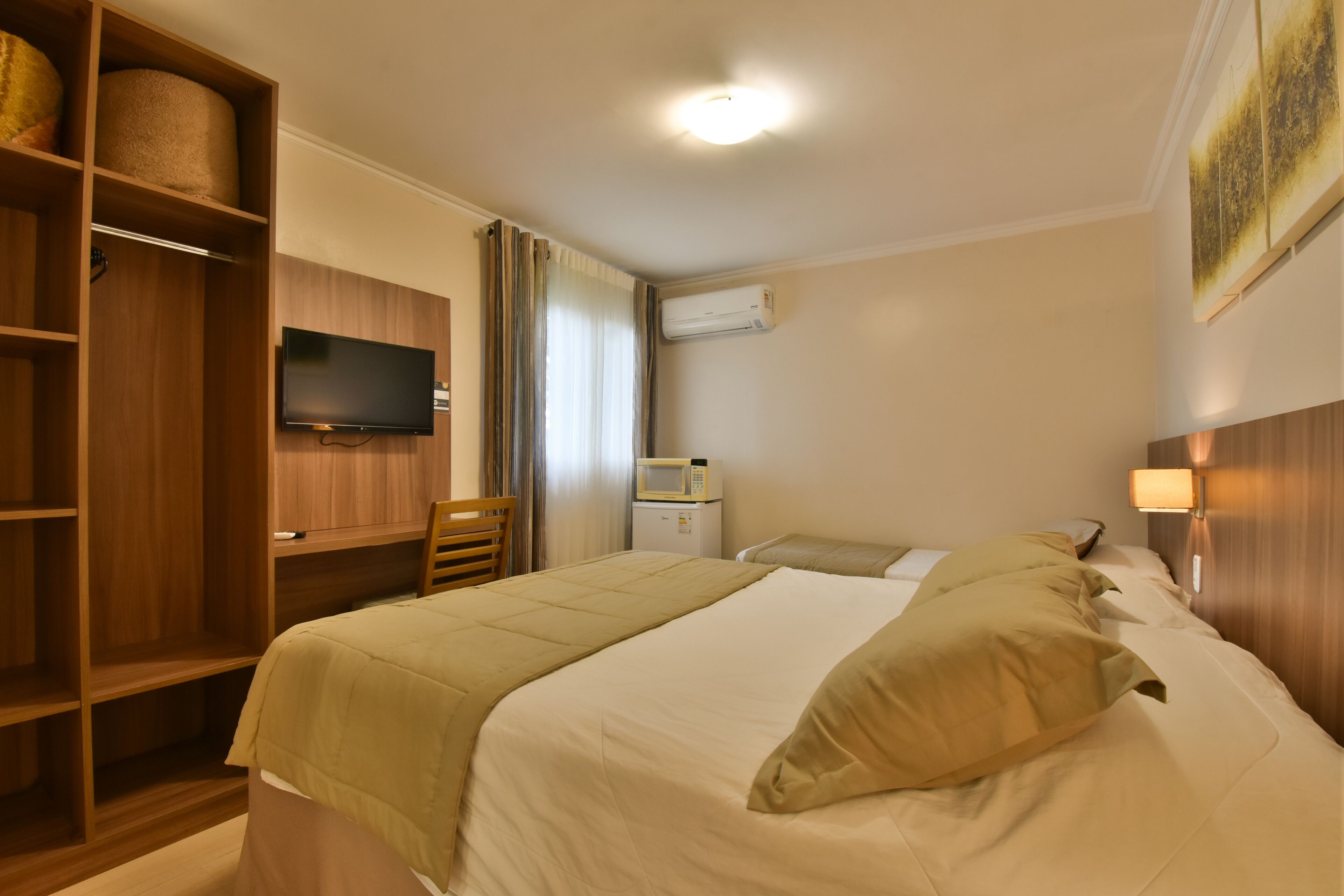 Una camera d'albergo con un letto, una televisione, un forno a microonde e un armadio.