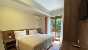 A hotel room with a bed, bedside tables, an air conditioning unit, a TV, and a view of greenery through a window. - Pousada Stillo Gramado (Gramado)
