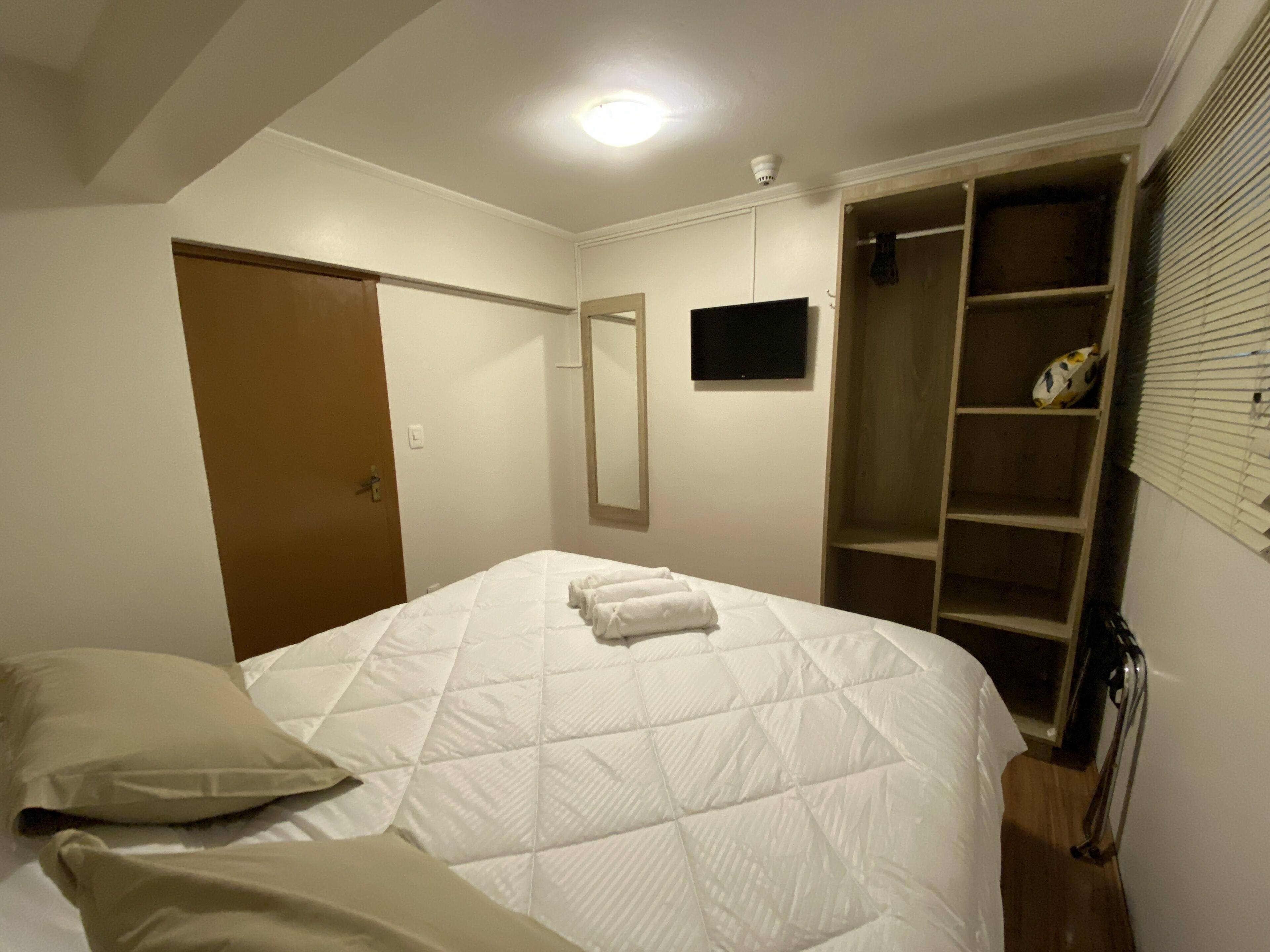 A bedroom with a bed, a wardrobe, a mirror, and a television.