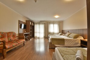 Habitación de hotel con sofá, dos camas, televisor, escritorio y armario.
