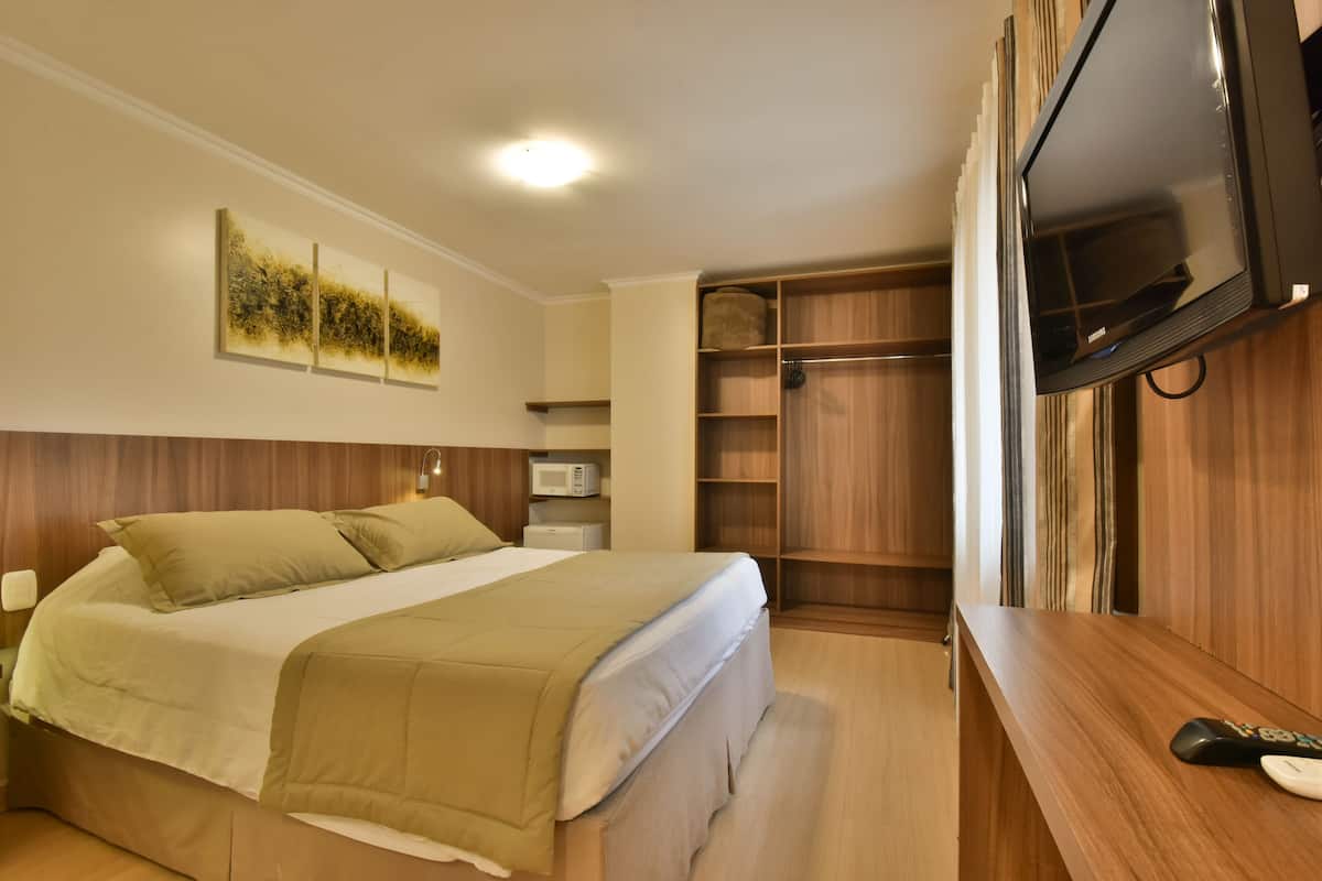 A bedroom with a bed, a TV, a microwave, and a wooden wardrobe.