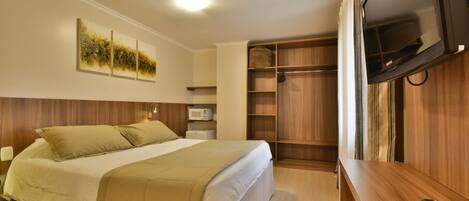 A bedroom with a bed, a TV, a microwave, and a wooden wardrobe.