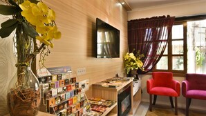 A reception area with a wooden reception desk, a flat-screen TV, a vase with yellow flowers, and two red chairs. - Pousada Stillo Gramado (Gramado)
