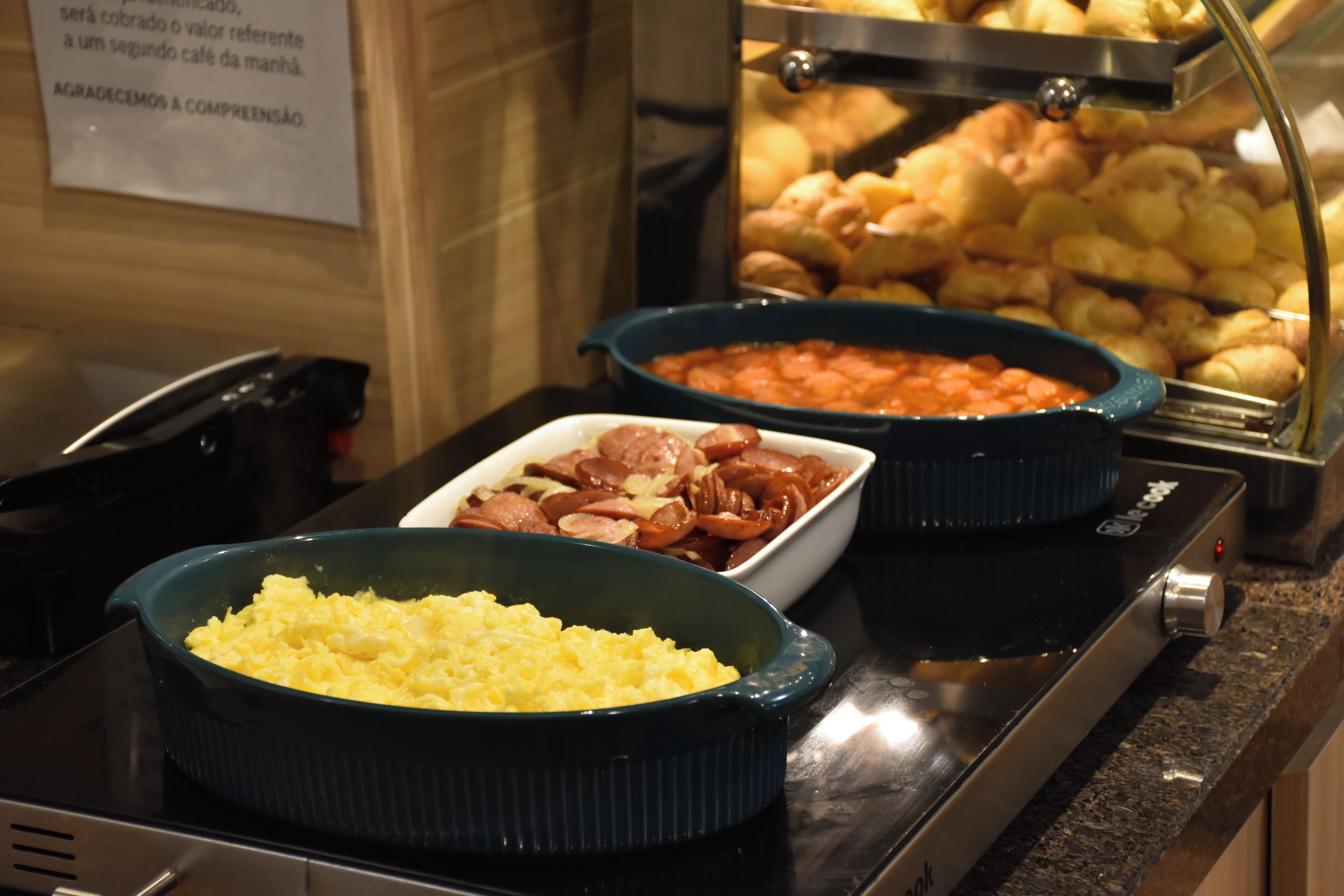 A buffet with various dishes including scrambled eggs, sausages, and baked potatoes.