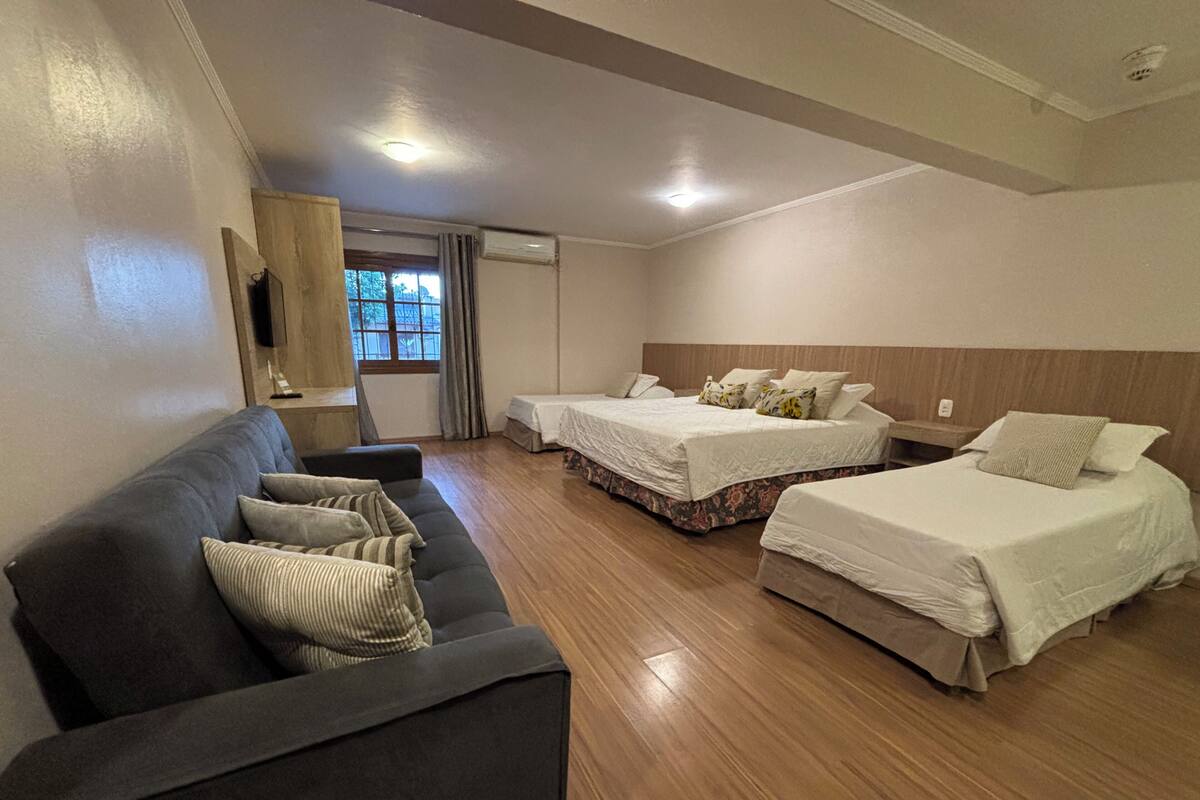A hotel room with two beds, a sofa, a wooden floor, and a window with curtains.