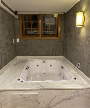Un baño con una bañera grande, una ventana con marcos de madera y un aplique de pared.