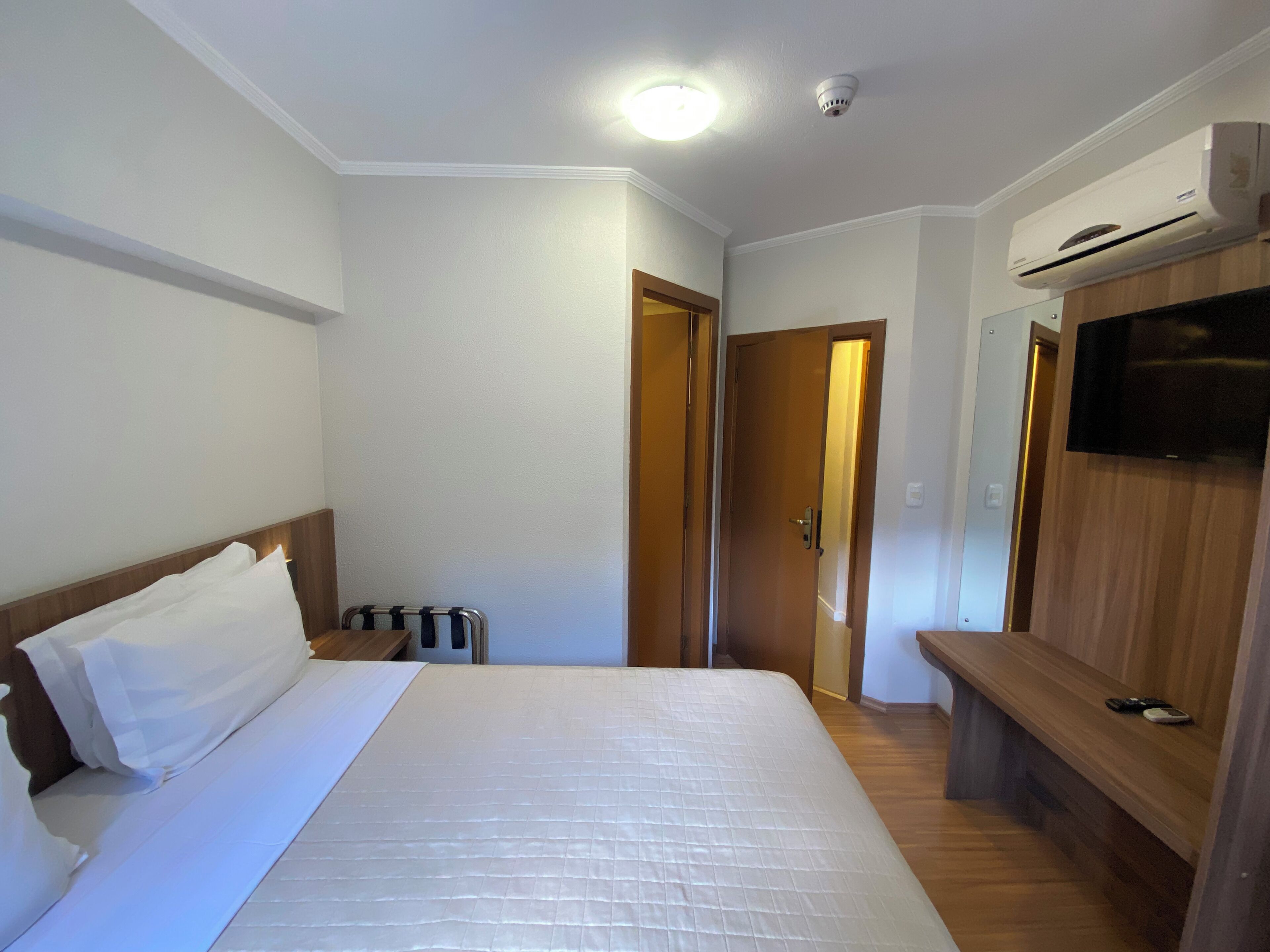 Une chambre d’hôtel équipée d’un lit, d’une télévision, d’une armoire et d’une porte donnant sur une autre pièce.