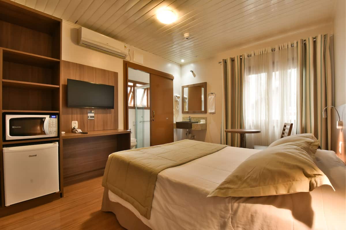 A hotel room with a bed, a TV, a mini-fridge, a microwave, and a bathroom with a shower.