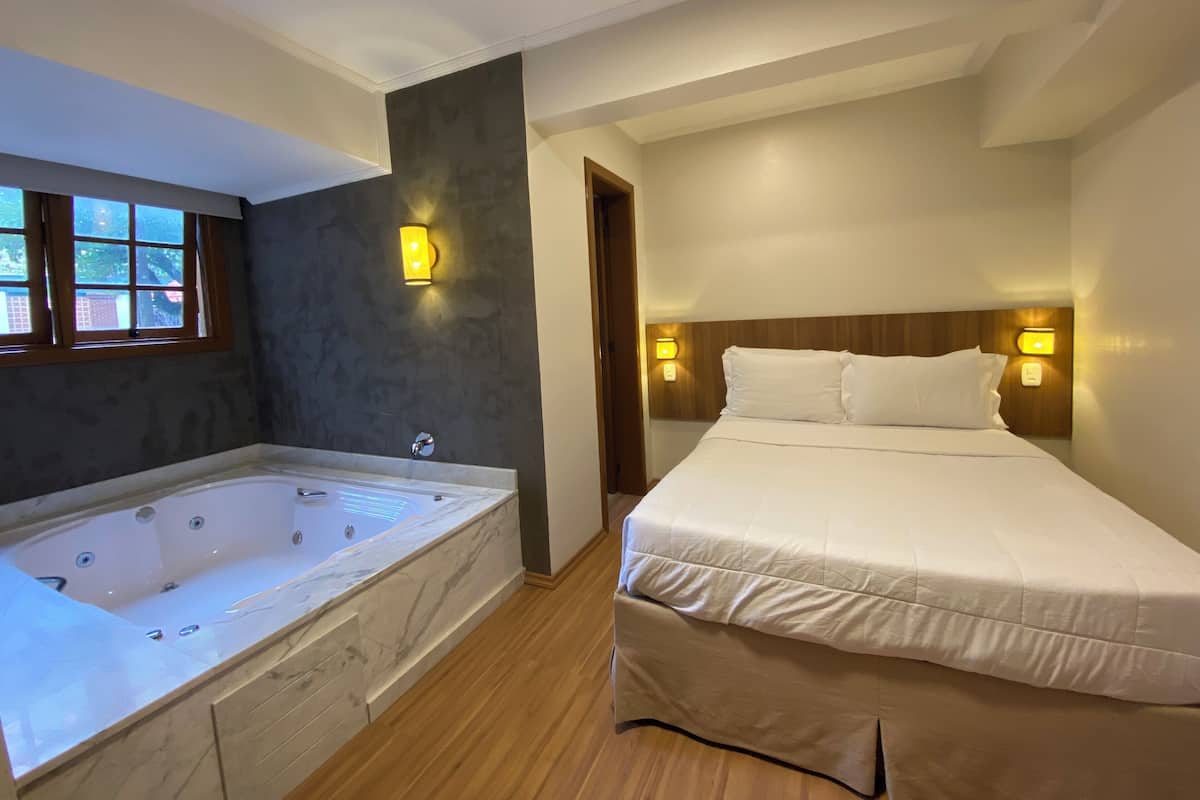 A room with a large bathtub, a bed with white bedding, and two wall-mounted light fixtures.