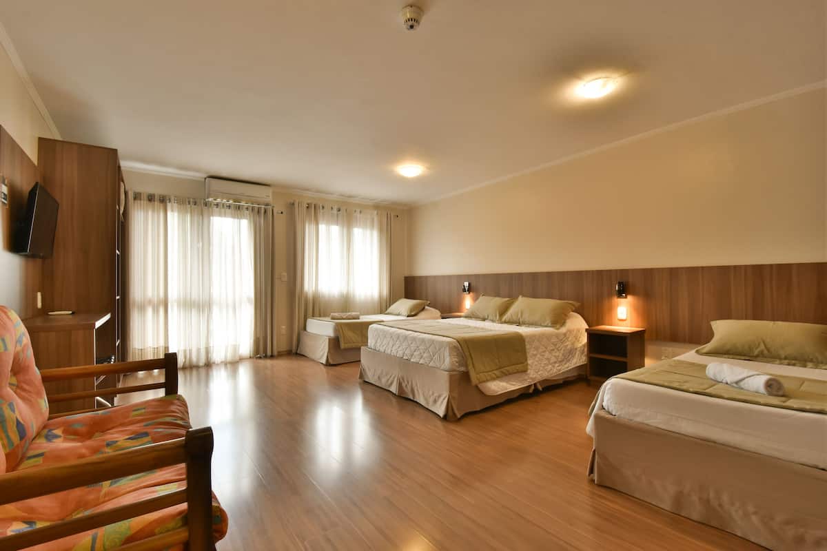 A hotel room with two beds, a wooden floor, a TV mounted on the wall, and a window with curtains.