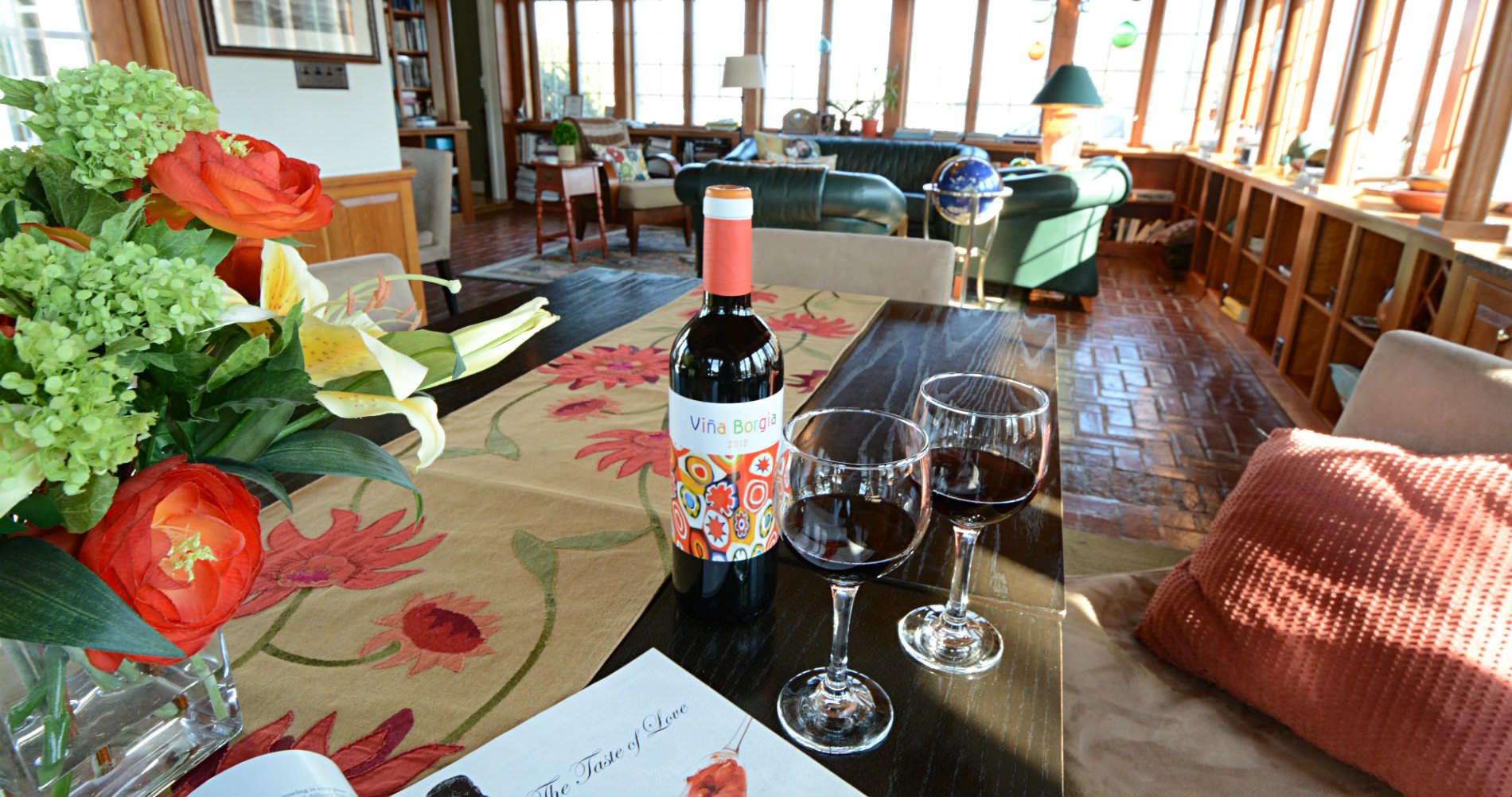 Una mesa con una botella de vino, dos copas de vino y un arreglo floral.