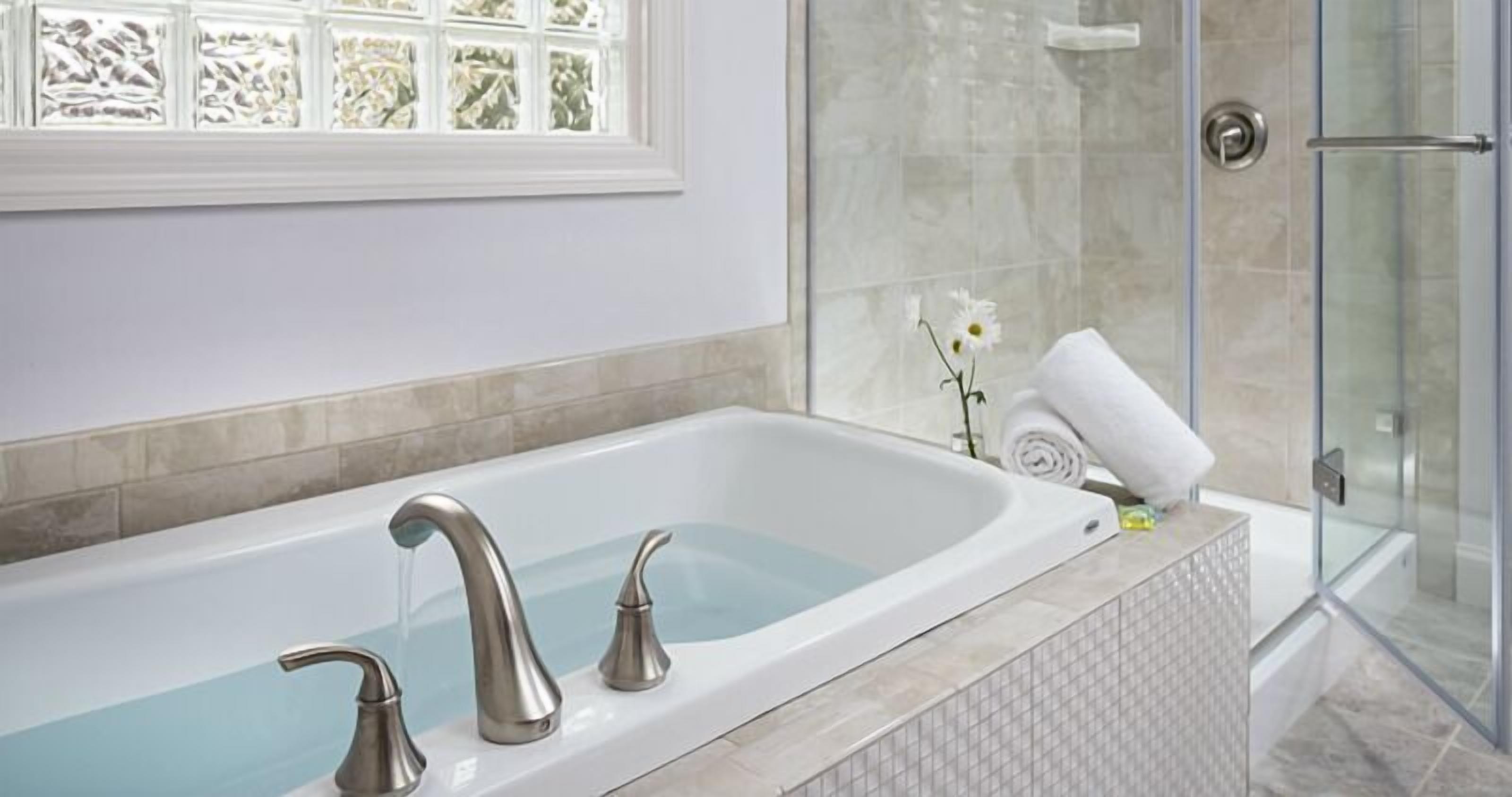 A modern bathroom with a freestanding bathtub, a glass shower enclosure, and a window with frosted glass panels.