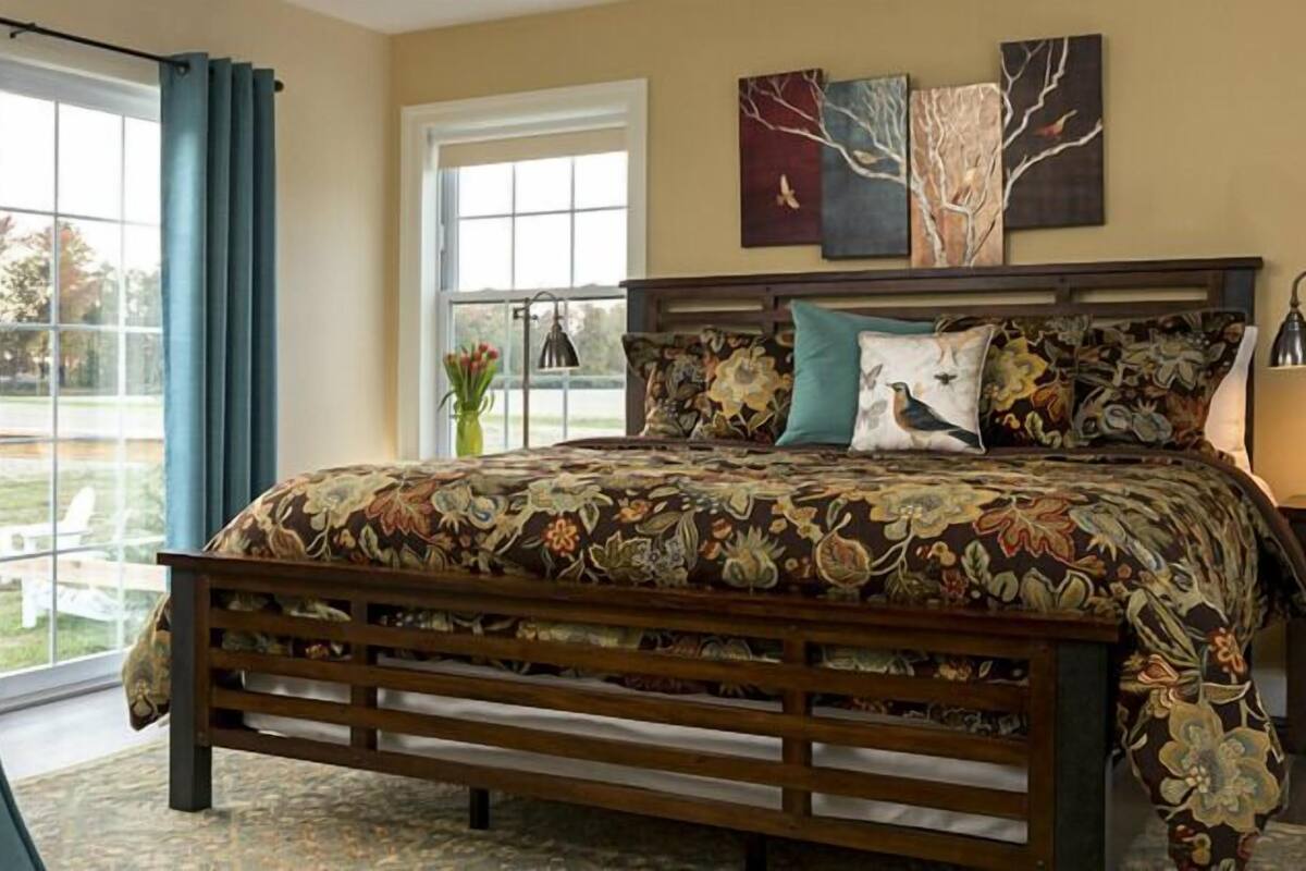 A bedroom with a large bed, a window, and artwork on the wall.