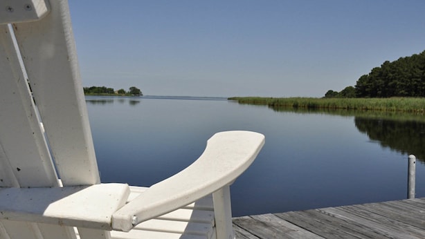 A boat deck with a white bench and a view of a calm lake and distant trees.