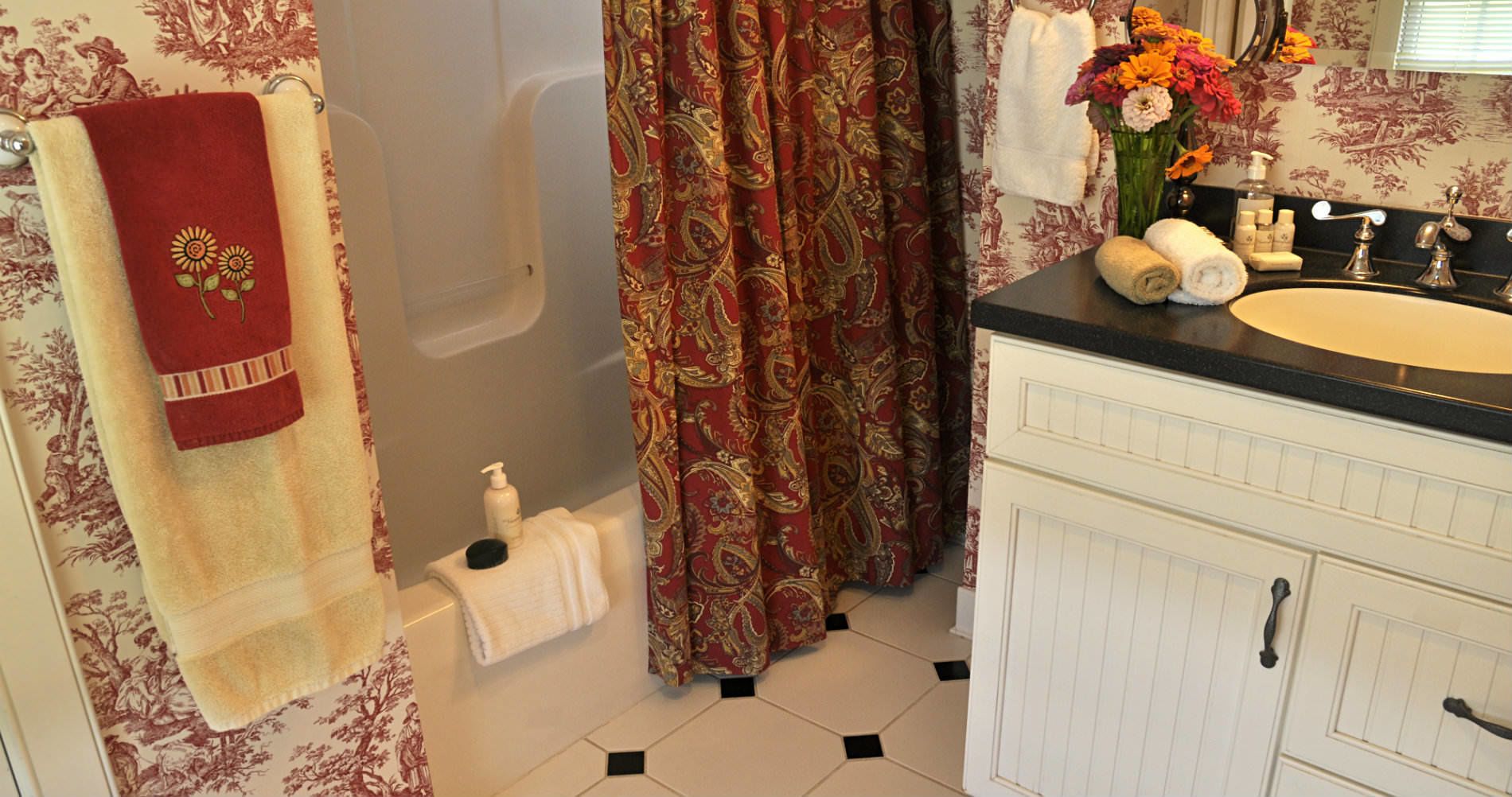 Une salle de bain avec une baignoire, un lavabo blanc avec un miroir et des toilettes. On y trouve des serviettes et des articles de toilette sur le comptoir.