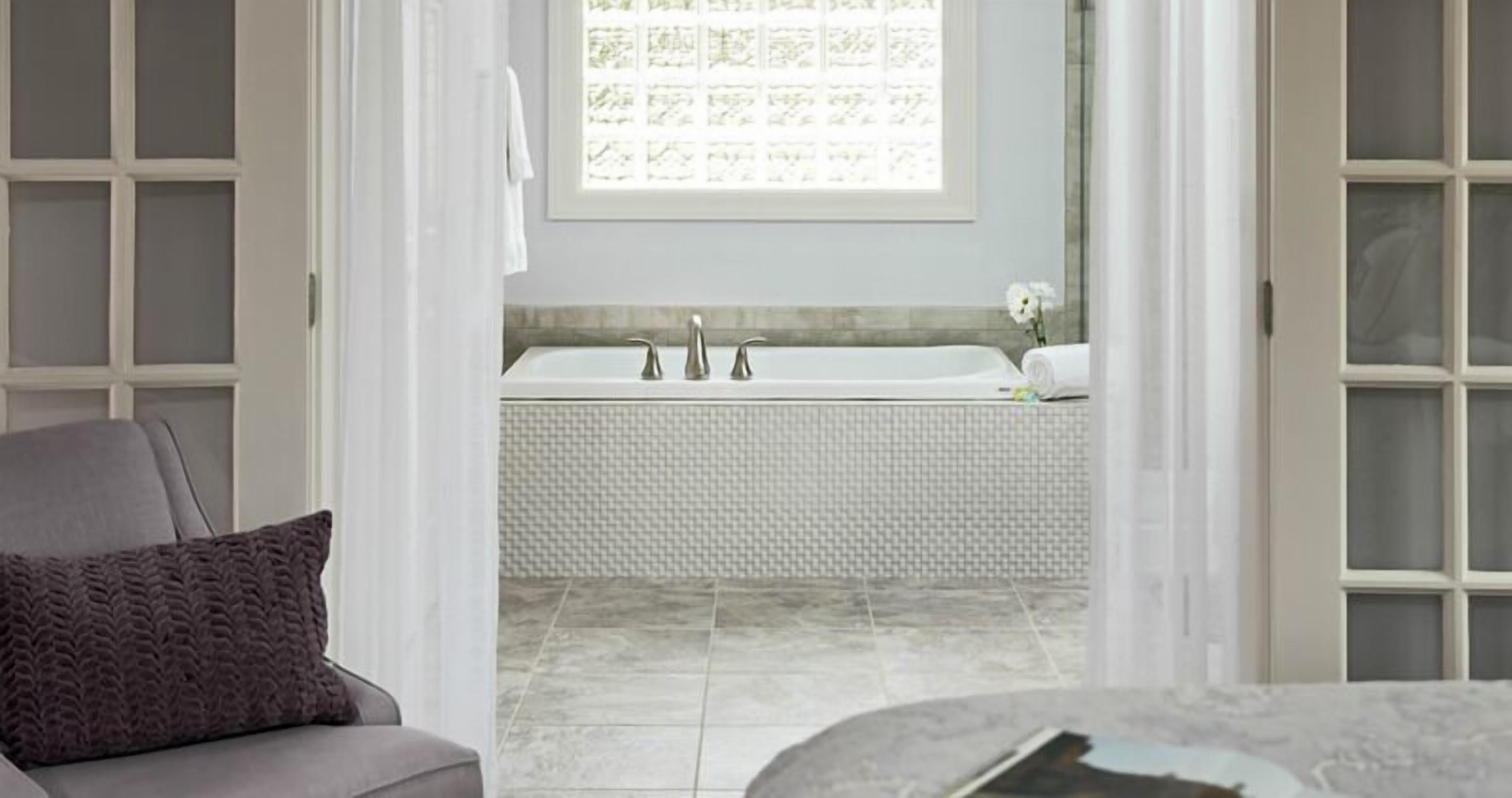 A bathroom with a white bathtub, a towel, and a window with a floral pattern.