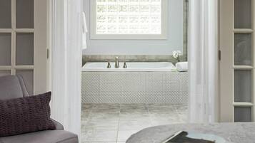 Un baño con una bañera blanca, una toalla y un ventanal con diseño floral.