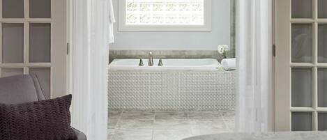 A bathroom with a white bathtub, a towel, and a window with a floral pattern.