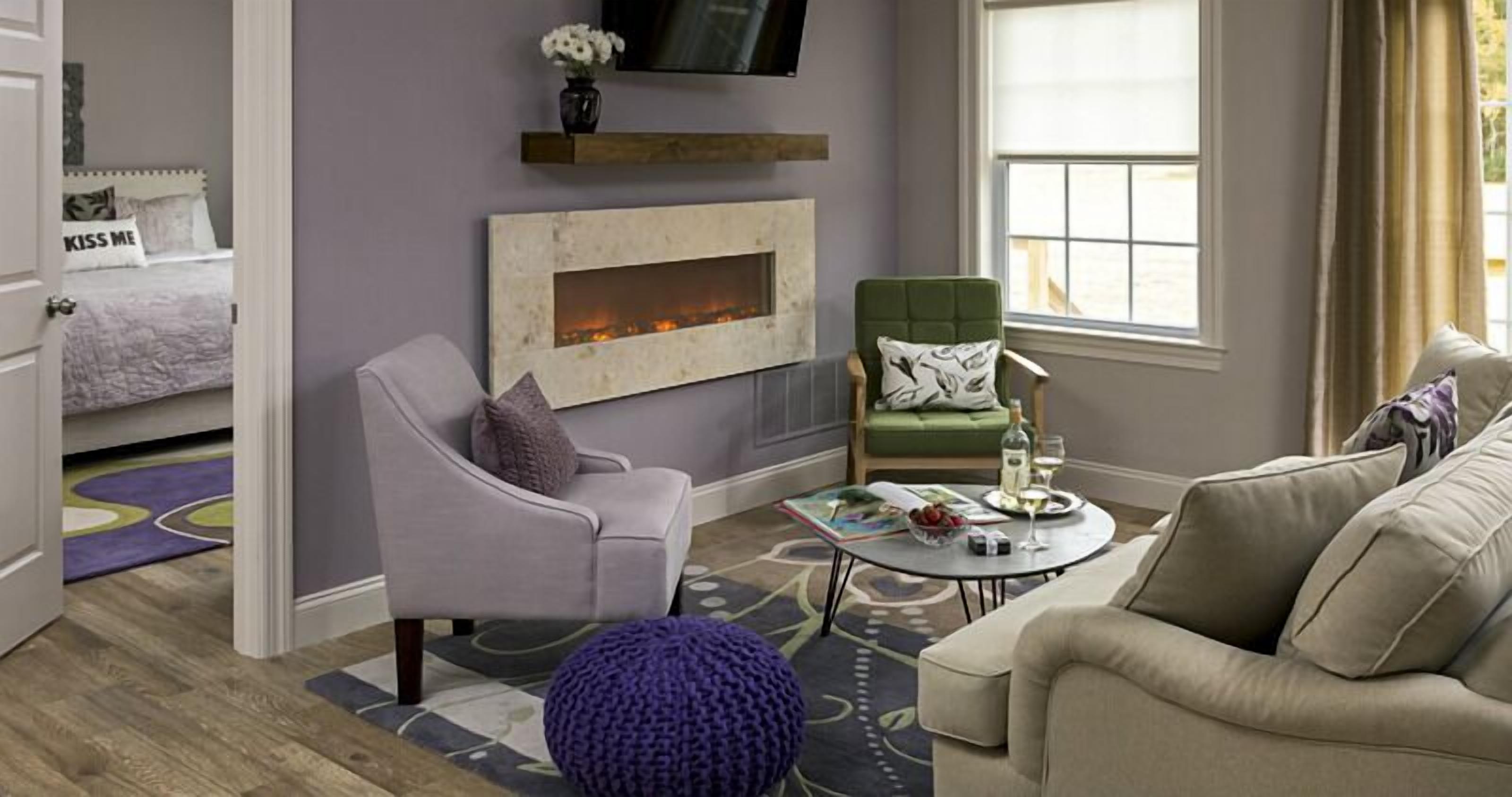 A living room with a fireplace, a green armchair, a beige sofa, and a coffee table with a magazine and a bottle.