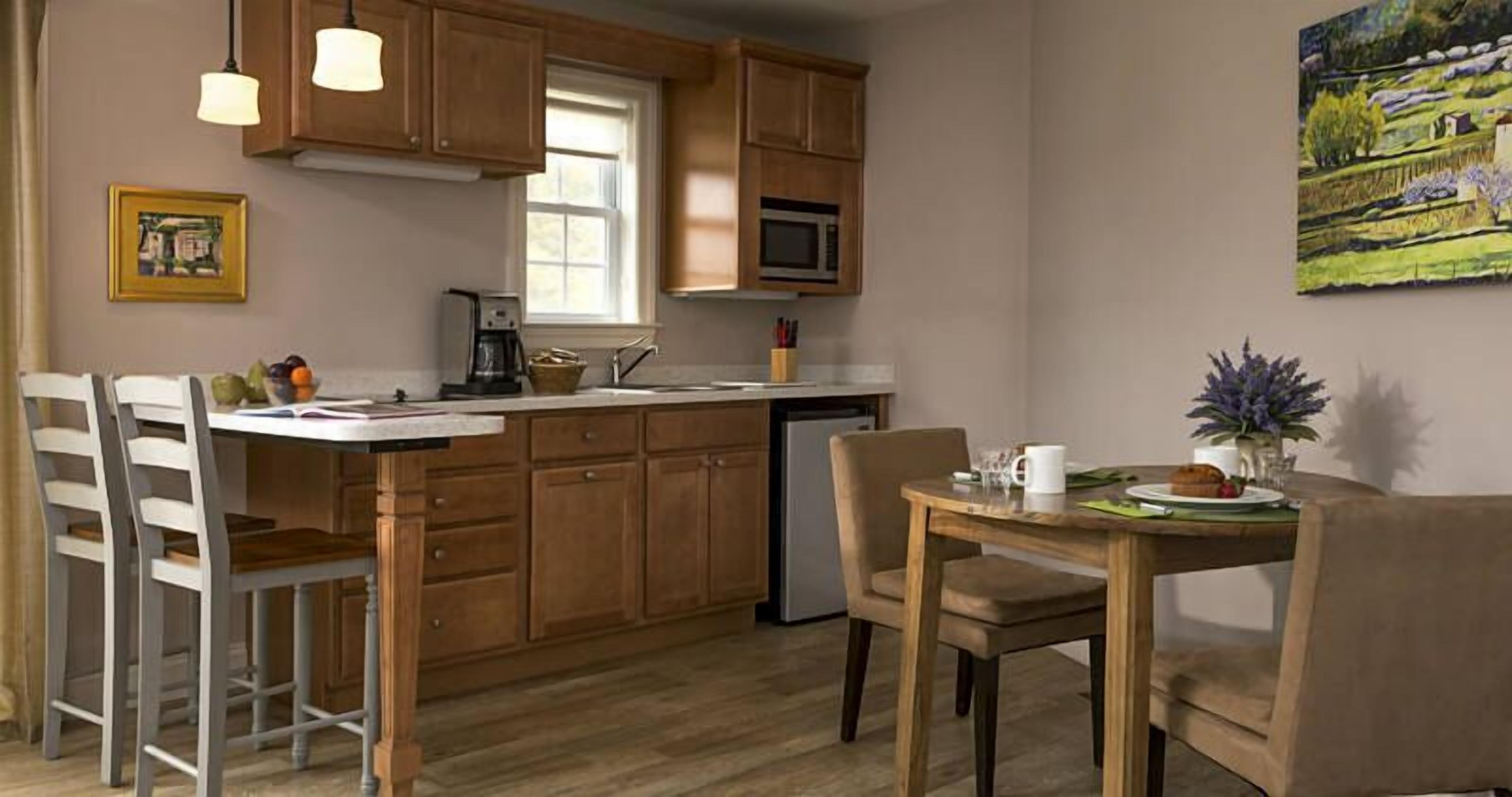 Una cocina con armarios de madera, microondas, cafetera y un comedor con sillas y mesa.