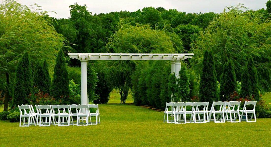 Allestimento per un matrimonio all'aperto, con sedie bianche e un pergolato bianco in un rigoglioso giardino.
