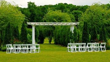 Allestimento per un matrimonio all'aperto, con sedie bianche e un pergolato bianco in un rigoglioso giardino.