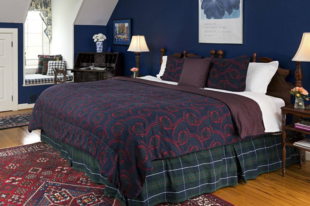 A bedroom with a large bed, a chair, a desk, and a window with curtains.