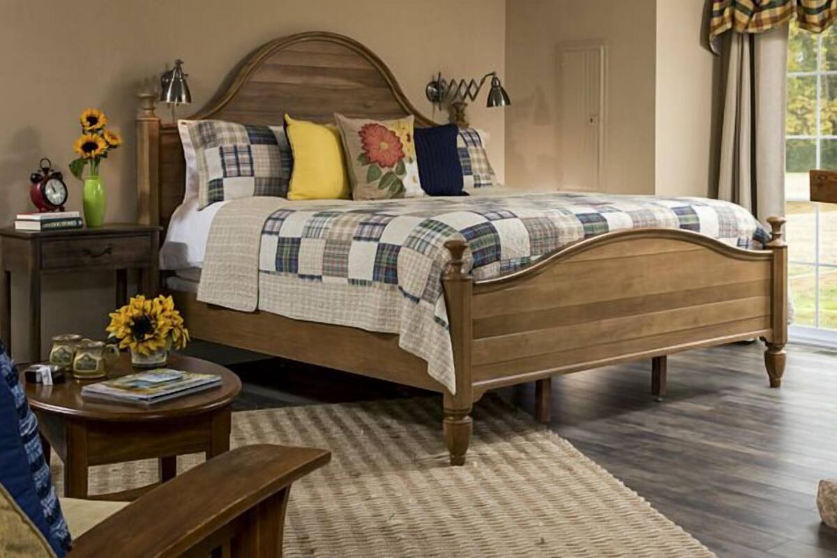 A bedroom with a wooden bed, a stone fireplace, a nightstand with a clock, and a vase with sunflowers.