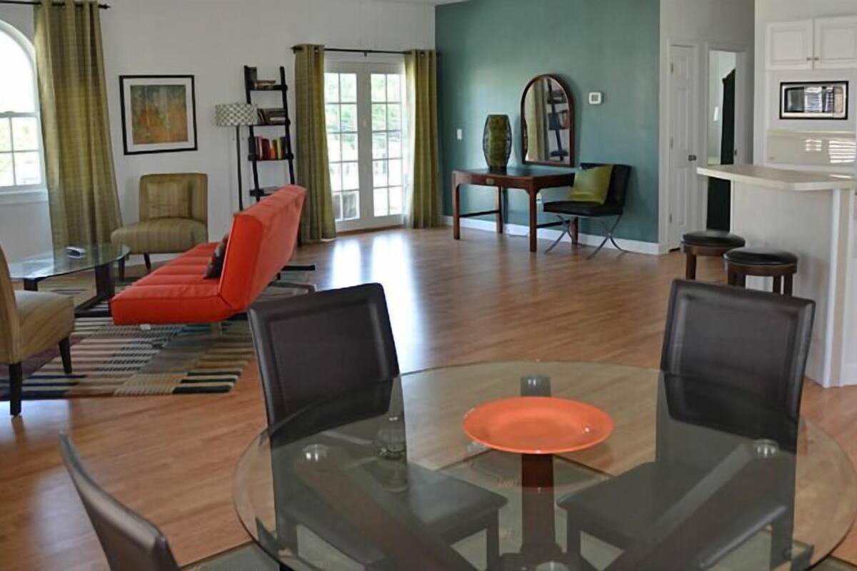 A modern living room with a glass dining table, a red sofa, and a kitchen area with white cabinets and appliances.