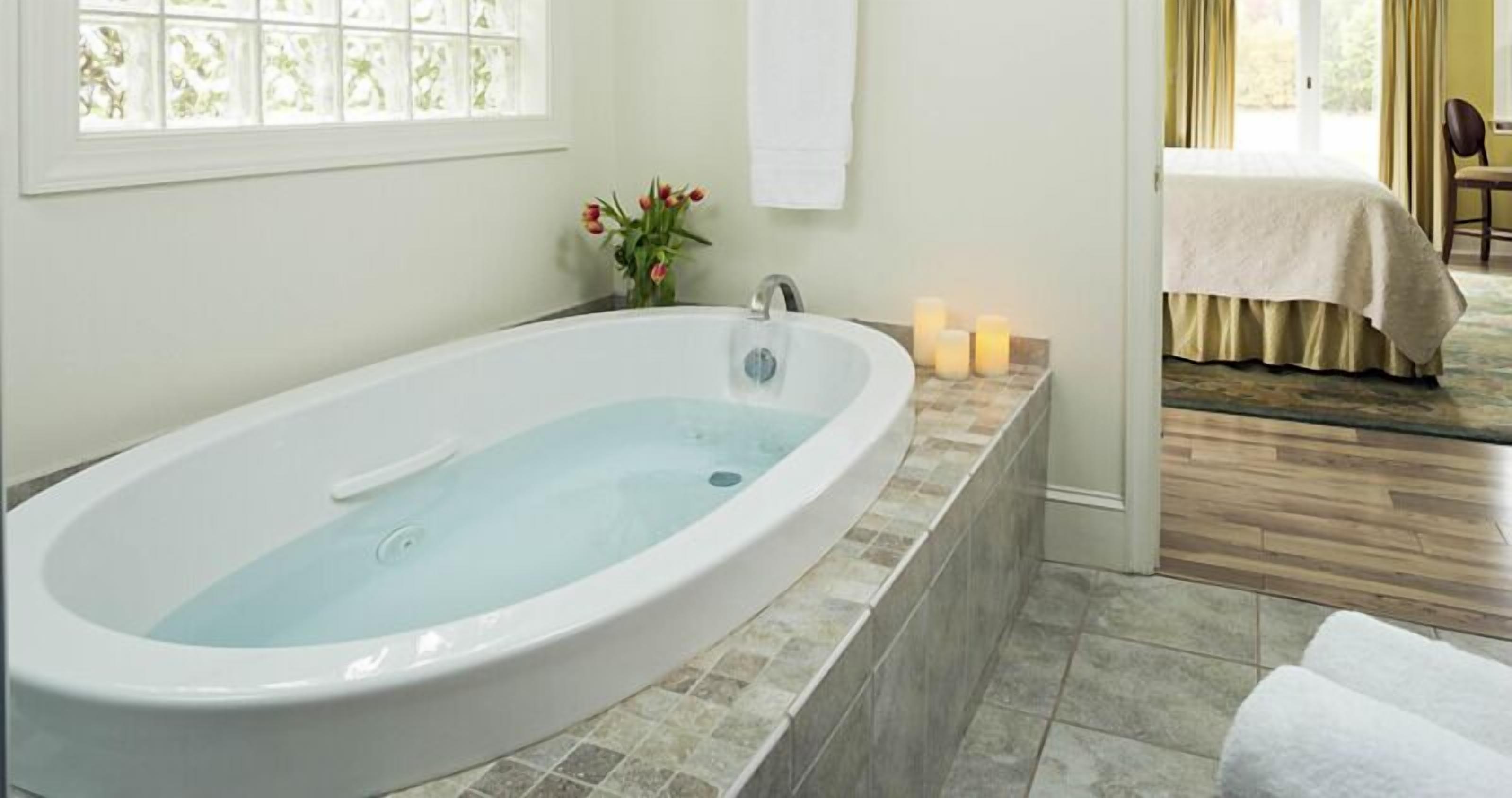 A modern bathroom with a freestanding bathtub, a window with frosted glass, and a small vase with flowers.