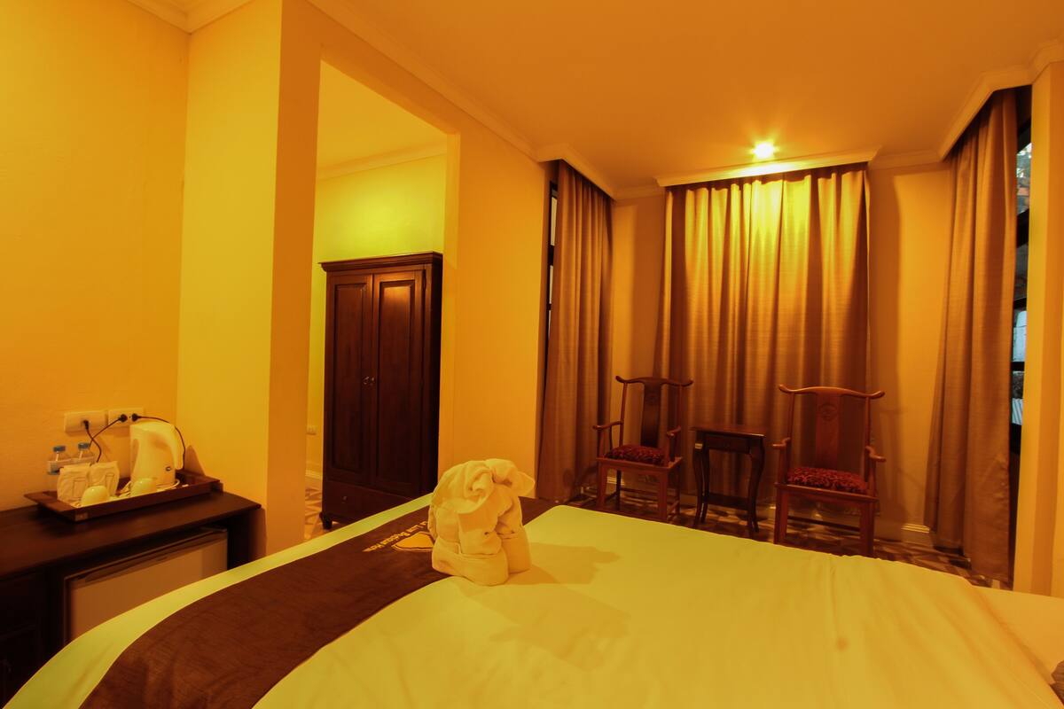 A hotel room with a bed, a desk with a coffee maker, a chair, and a wardrobe.